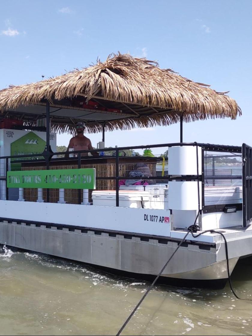 Floating tiki bar with a thatched roof on calm water, blue sky in background.