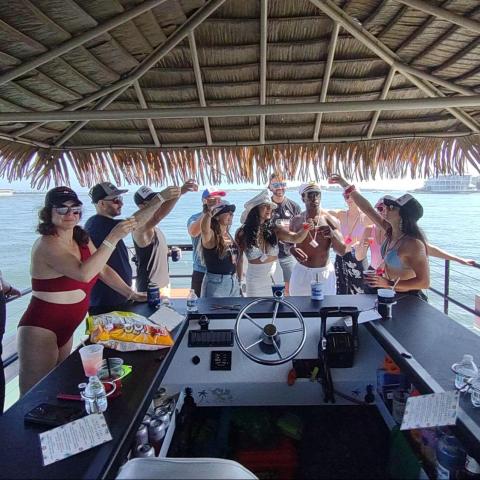 Group of people on a boat with a thatched roof enjoying a drink near the water.