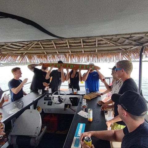 Group of people on a tiki boat having drinks and socializing on a sunny day.