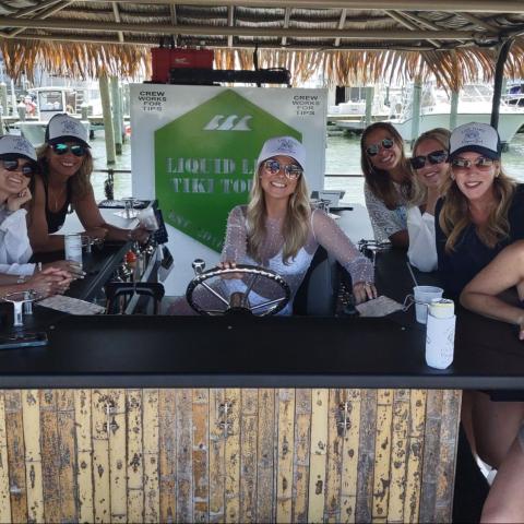 Group of eight women smiling on a tiki boat by a marina.