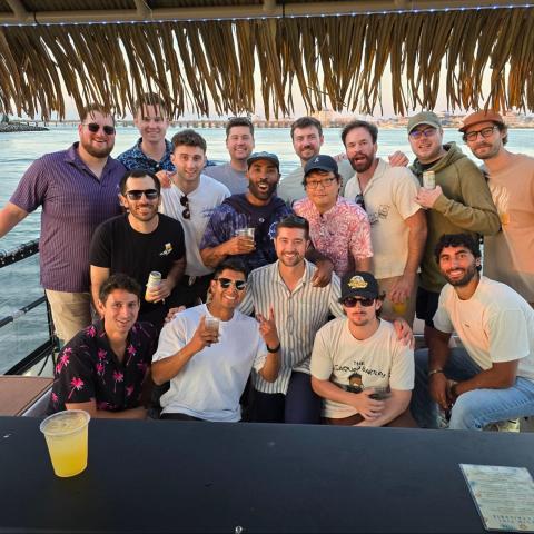A group of friends on a boat with drinks, wearing casual summer attire.