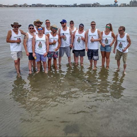 Group of people in matching tank tops standing in shallow water on a beach.