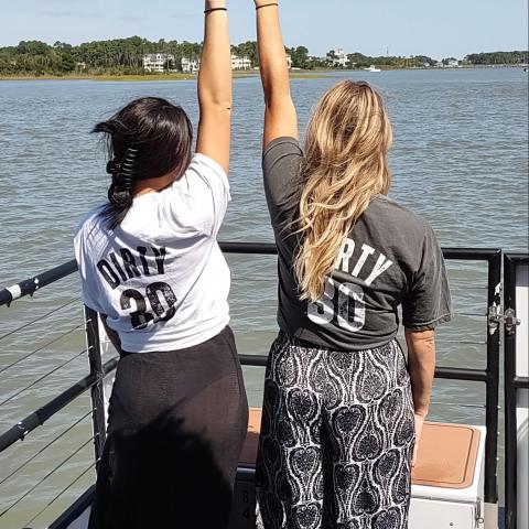 Two people on a boat with hands raised, wearing shirts saying 'Dirty 30'.
