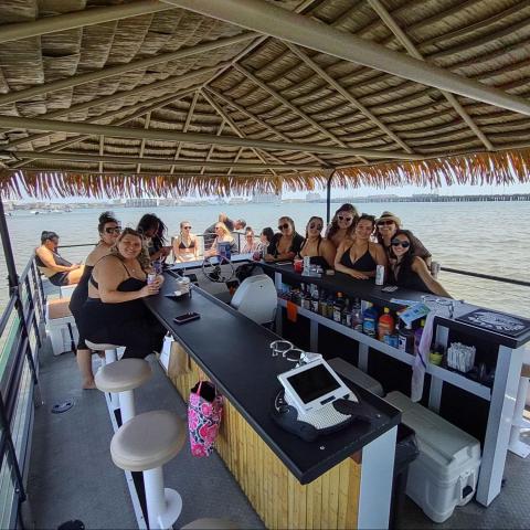 Group of people on a tiki bar boat on a sunny day near the water.