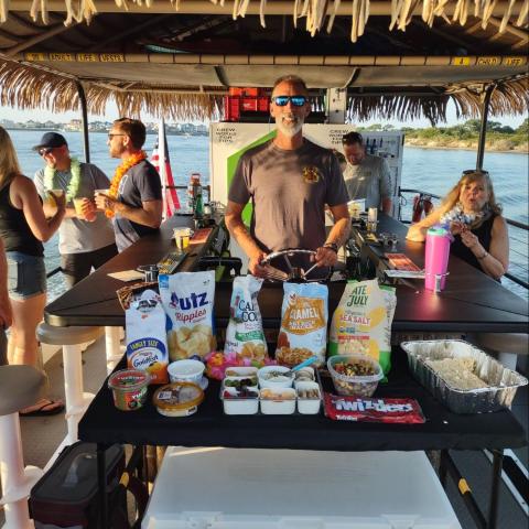 People on a boat with snacks displayed on a table under a thatched roof.