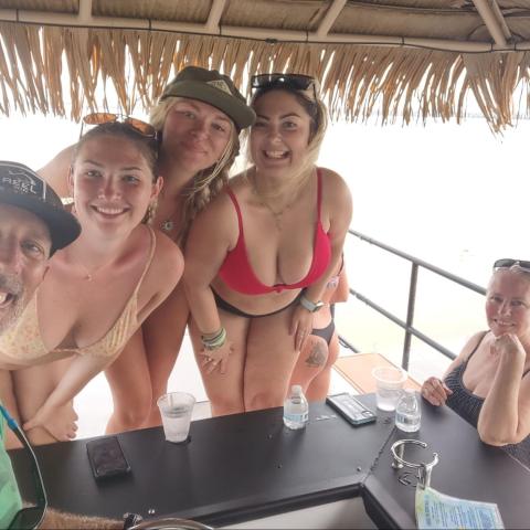 Group of people smiling under a thatched roof, with drinks on a counter.