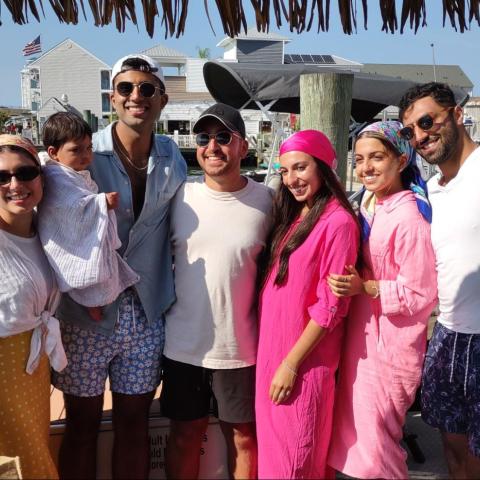 Group of people smiling on a dock with boats and a building in the background.