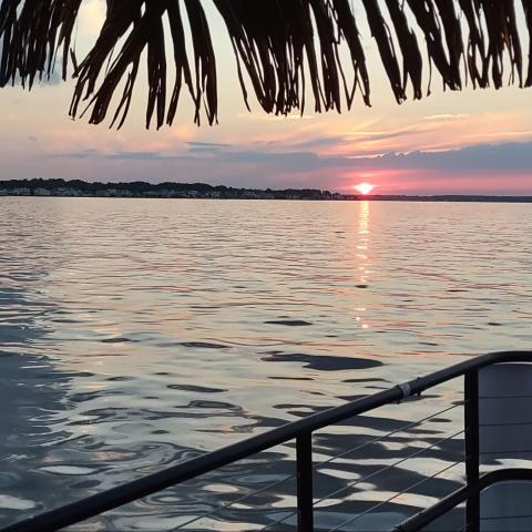 Sunset over a calm lake with a thatched roof and railing in the foreground.